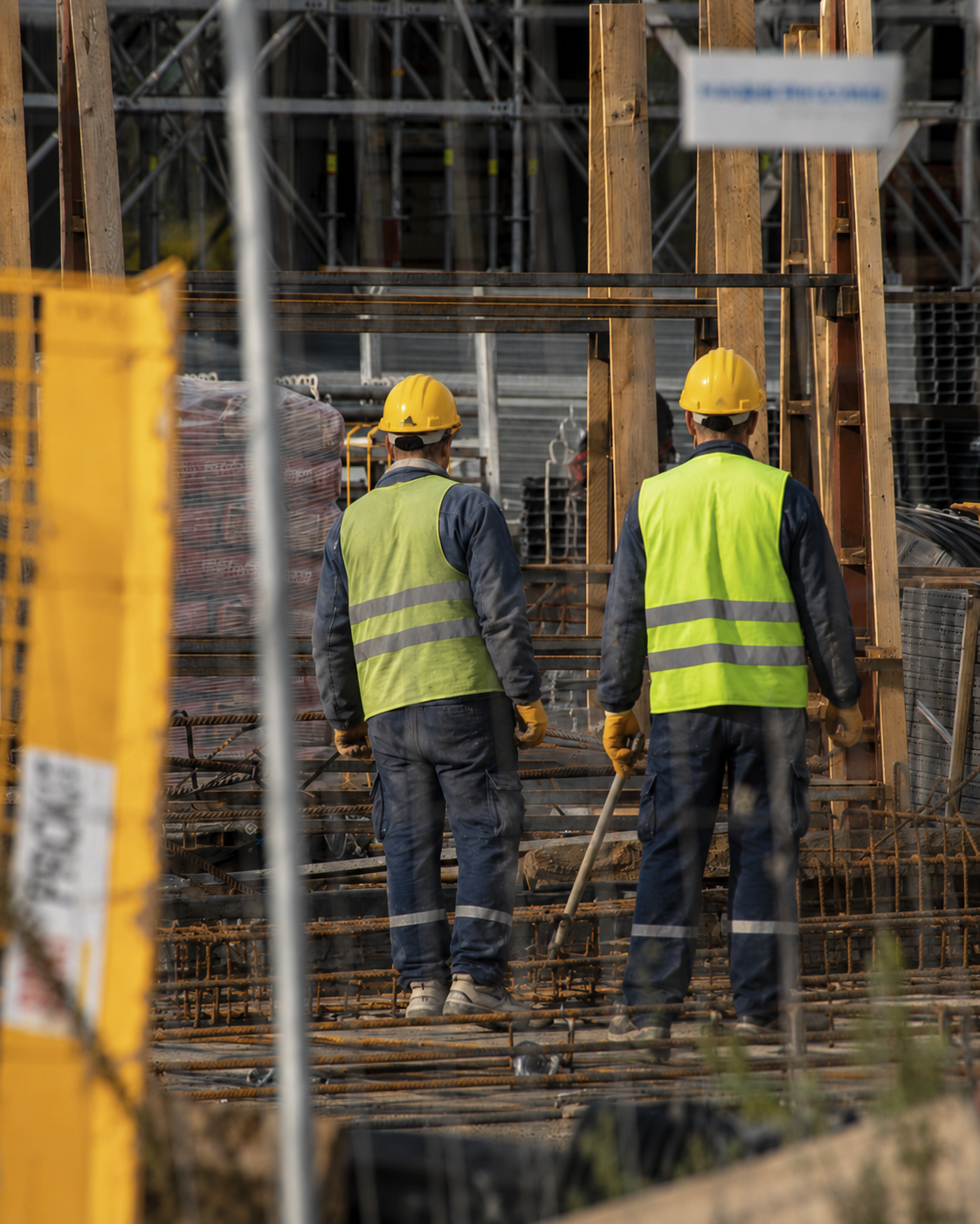 Two construction workers in safety gear collaborate efficiently in a busy construction site